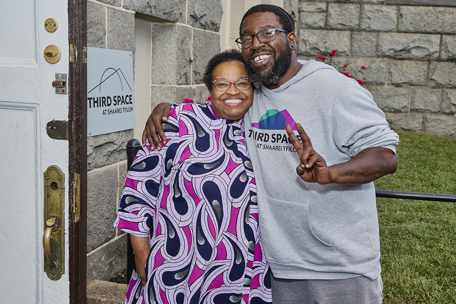 Two people hug outside Third Space, one wears a Third Space hoodie.