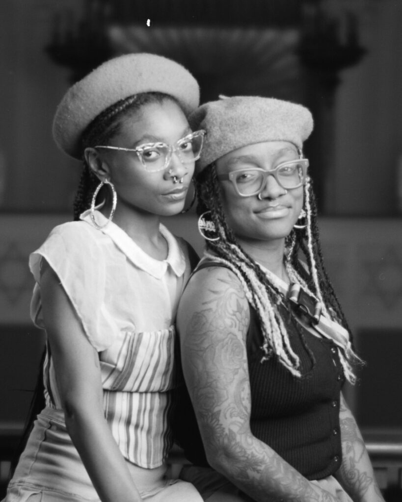 Black and white photo of two people in hats smiling at the camera