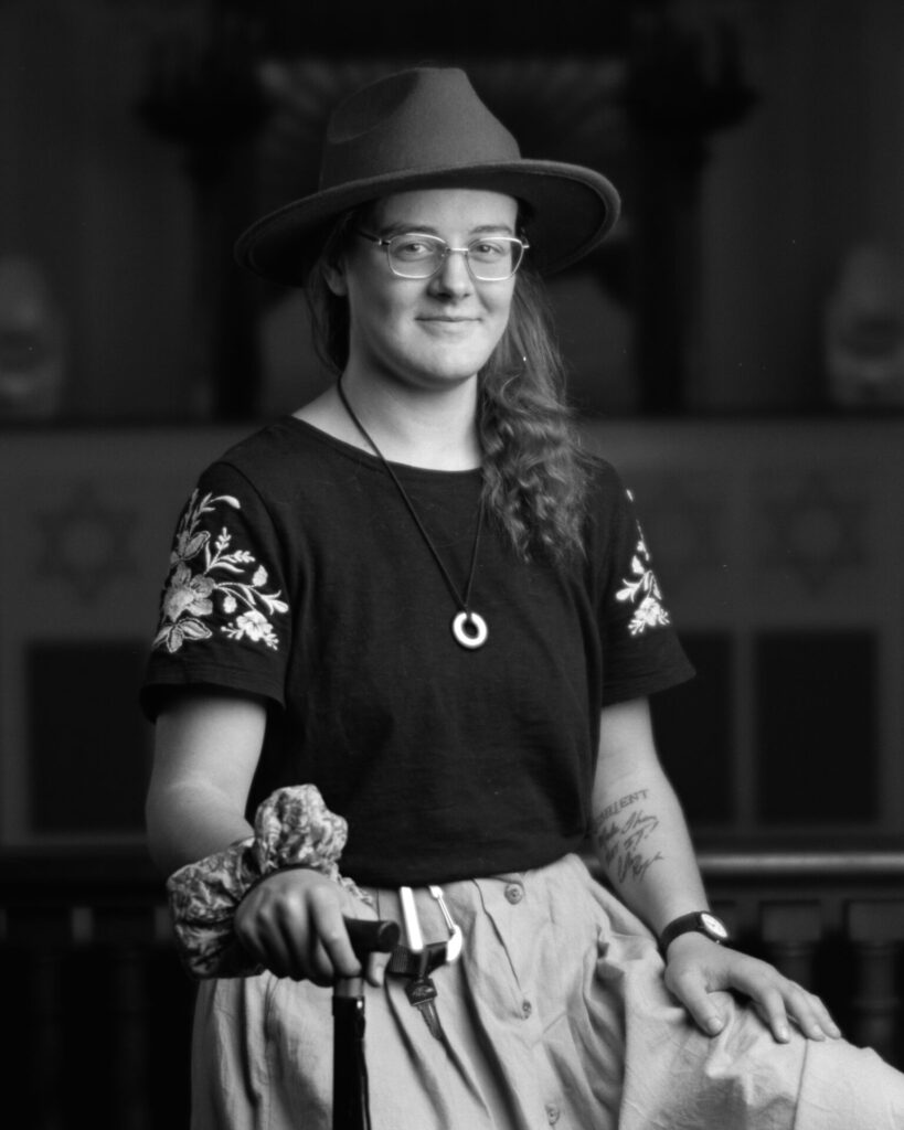 Black and white photo of a person in a hat smiling at the camera with one hand on a cane