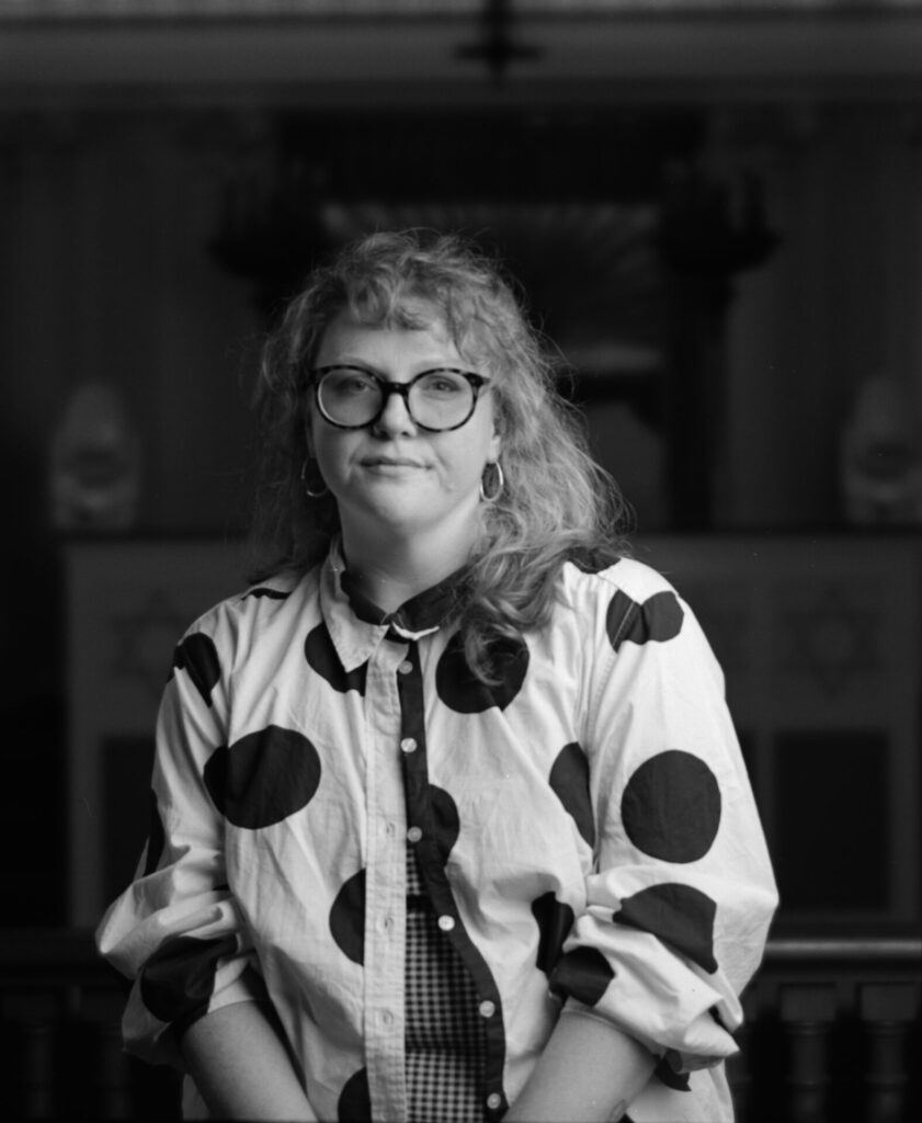 Black and white photo of a person wearing a jacket with large polka dots looking directly at the camera.