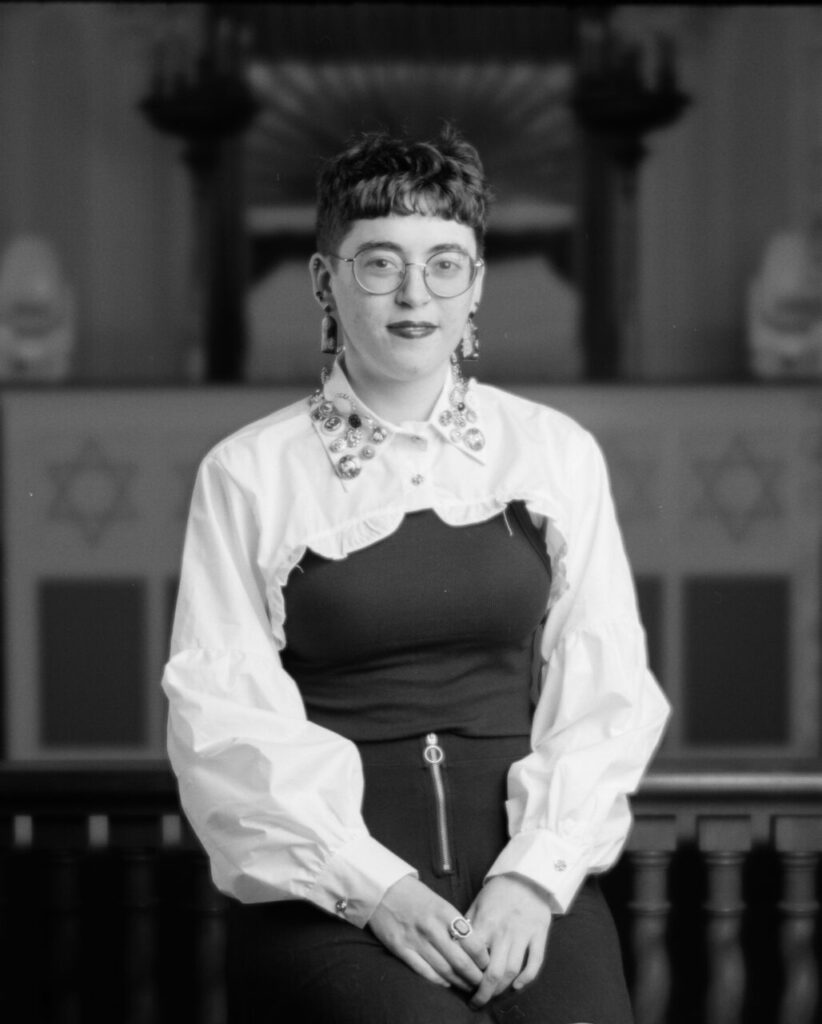 Black and white photo of a person in a black and white outfit looking directly at the camera