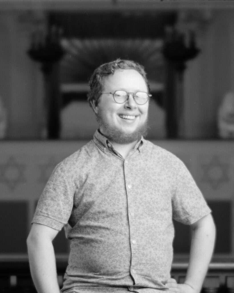 Black and white photo of a person with a beard and glasses smiling at the camera