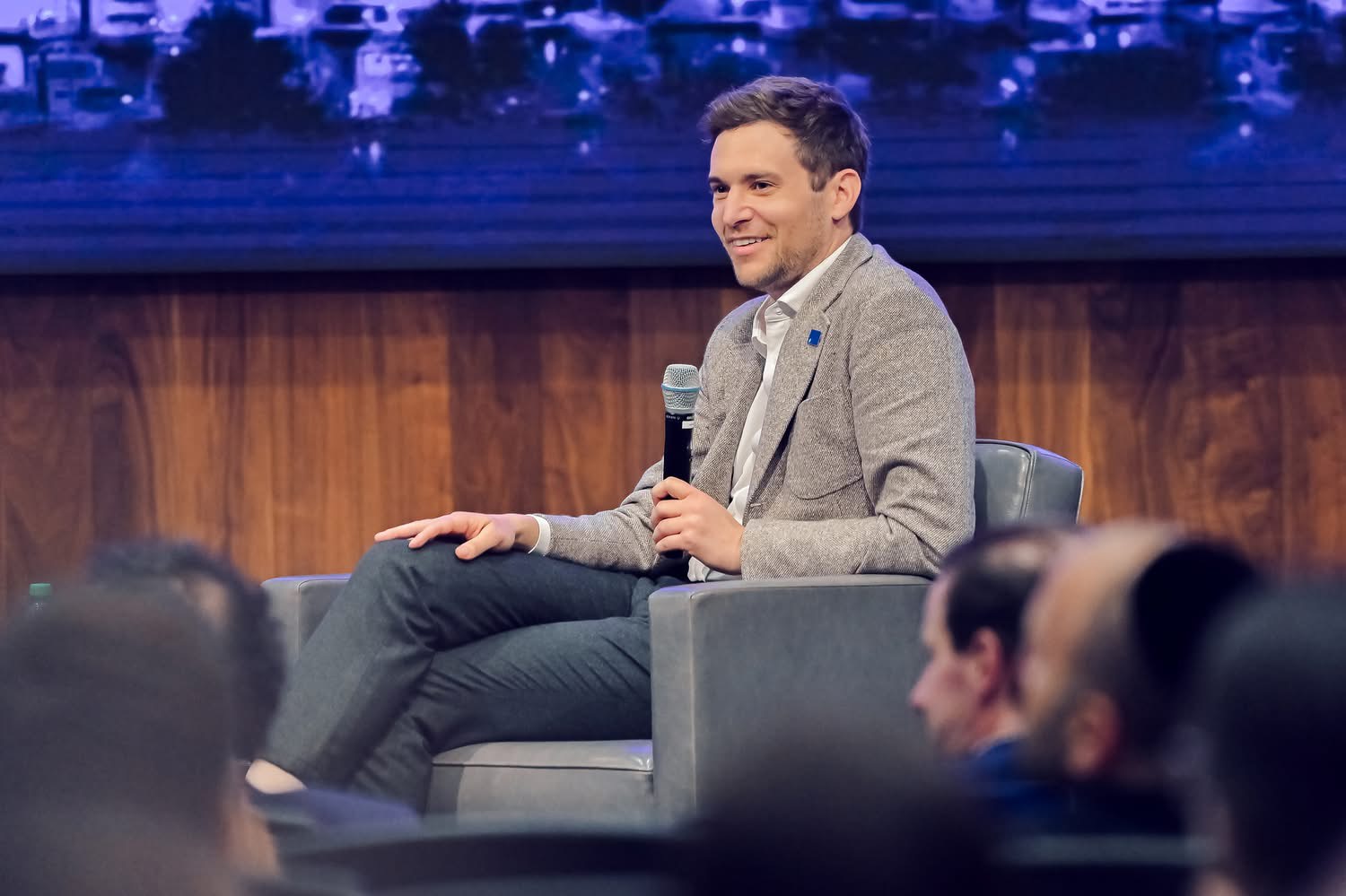 Adam Neuman seated on the set of a tv show, microphone in hand