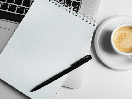 A blank notebook sitting on top of a laptop keyboard next to a cup of coffee.