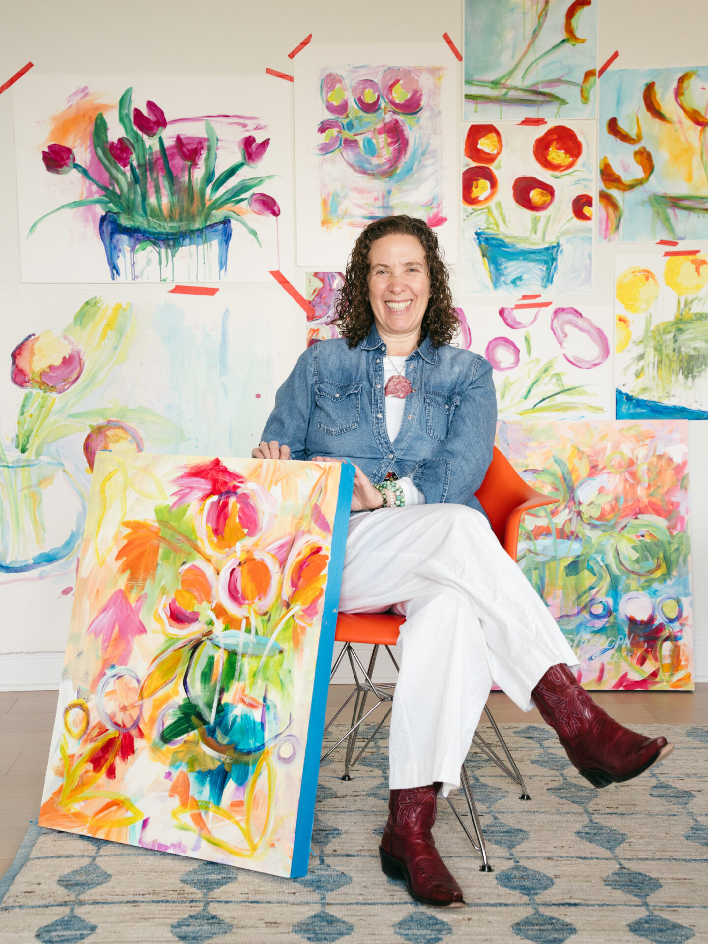 Emily Gaines Demsky seated and smiling surrounded by colorful paintings of flowers